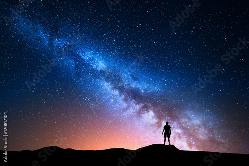 Milky Way. Beautiful night sky with stars and silhouette of a standing alone man on the mountain. Milky way with red light and man on the hill. Background with galaxy and silhouette of a man. Universe