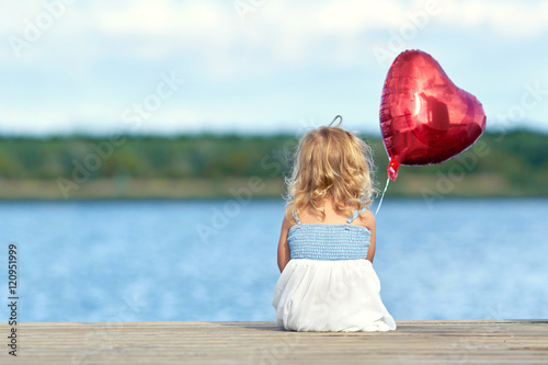 kleines Mädchen sitzt am Steg mit roten Ballon