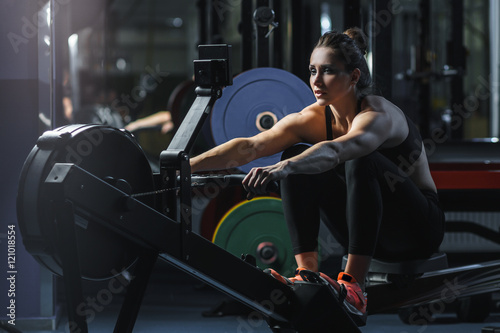 Concept: power, strength, healthy lifestyle, sport. Powerful attractive muscular woman CrossFit trainer do workout on indoor rower at the gym