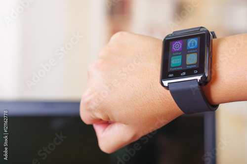 Closeup arm wrist wearing smart watch, screen lit up, using other hand pressing on device, white studio background