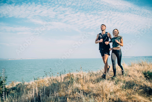 Young couple running outdoor. Male and female jogging in the countryside near the lake