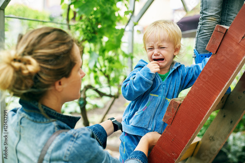 Little boy crying looking at the mother standing on the stairs