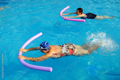 Two senior women doing swimming exercise in pool.