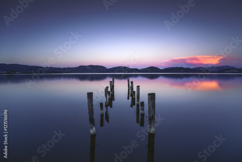 Wooden pier or jetty remains on a blue lake sunset and sky refle