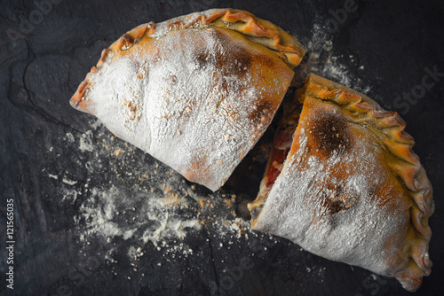 Sliced calzone with flour on the dark stone background top view