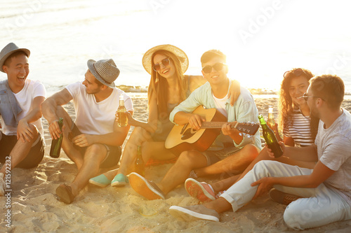 Group of friends listening to guitar and drinking beer at beach
