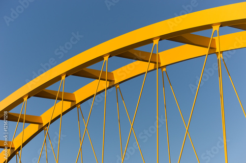 Yellow bridge against a steel blue sky showing beams, girders, columns and cables