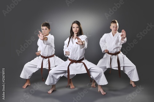 One female and two male brown belt karate doing kata on the gray background