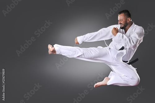 Handsome young black belt male karate doing kick on the gray bac