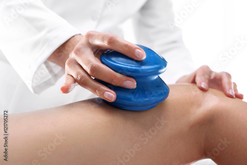 Masaż odchudzający, modelowanie sylwetki. Kosmetyczka masuje uda kobiety gumowymi bańkami do masażu.