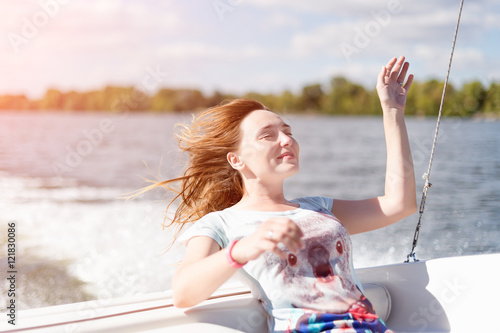 Relaxed young woman with closed eyes of pleasure sitting on sailboat, enjoying mild sunlight, sea or river cruise, summer vacation and travel concept.