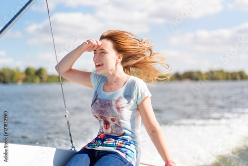 Smiling young woman sitting on sailboat, enjoying mild sunlight, sea or river cruise, summer vacation and travel concept.