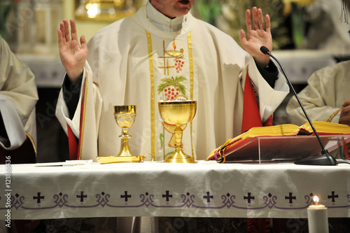 Golden chalices on the altar with priest in the background.