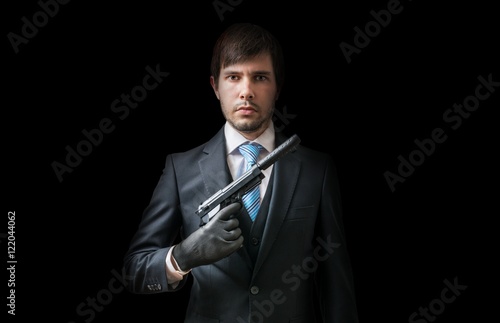Hitman or murderer with pistol with silencer on black background. Low key photo.