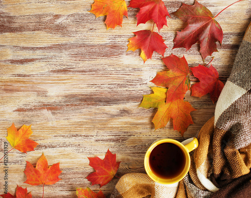 Cup of tea with plaid and leaves on the wood background.