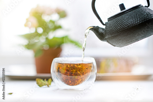 Herbal tea pouring from teapot to glass cup