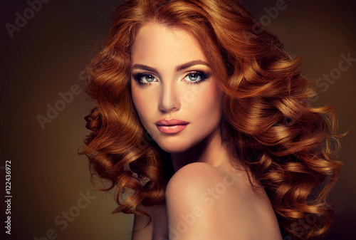 Girl with long and shiny wavy red hair . Beautiful model with curly hairstyle .