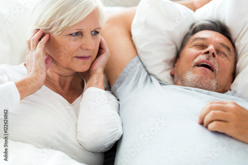 Senior man snoring and woman covering ears 