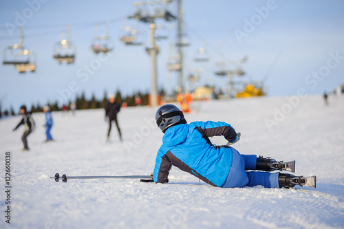 Young woman skier in blue ski suit after the fall on mountain slope trying get up against ski-lift. Ski resort. Winter sports concept.