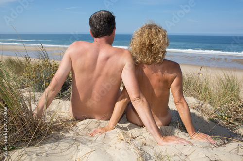 Relaxing nudist couple sitting on beach under deep blue sky