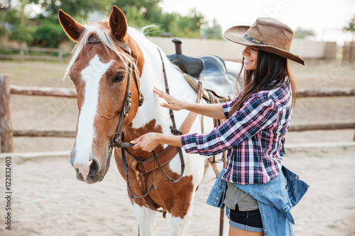 Happy woman cowgirl taking care of her horse on ranch