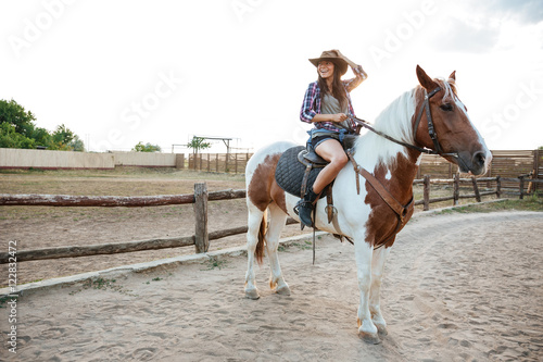 Smiling woman cowgirl sitting and riding horse on ranch