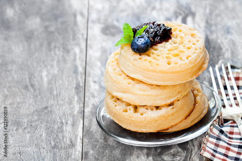 Hot toasted crumpets on the wooden table with blueberries and j