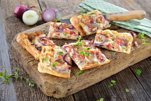 Elsässer Flammkuchen mit Zwiebeln und Speck rustikal auf altem Schneidbrett serviert - Traditional Alsatian tarte flambée with onions, bacon and sour cream served on a shabby cutting board