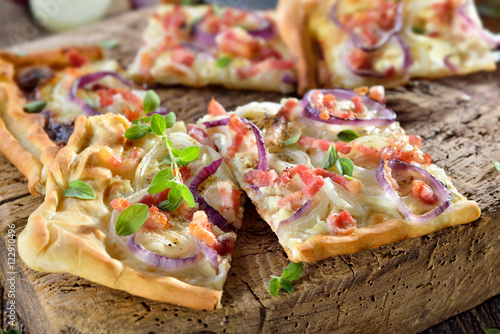 Elsässer Flammkuchen mit Zwiebeln und Speck rustikal auf altem Schneidbrett serviert - Traditional Alsatian tarte flambée with onions, bacon and sour cream served on a shabby cutting board