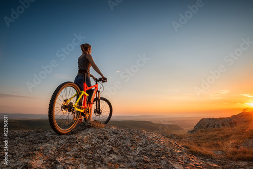 Sunset from the top / A woman with a bike enjoys the view of sunset over an autumn forest