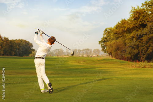 Boy golf player hitting by iron from fairway at autumn evening