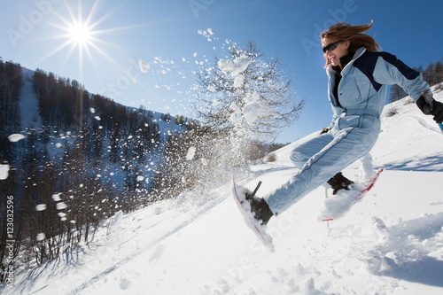 femme riant qui saute dans la neige avec des raquettes