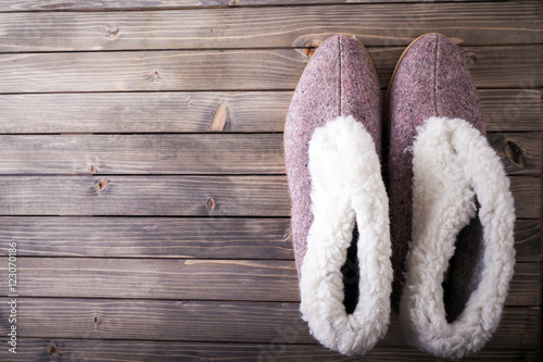 Shoes - A pair of fluffy sheep skin bedroom slippers on a rustic wooden floor board background