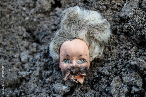 Melted plastic girl doll head lie in a pile of ash
