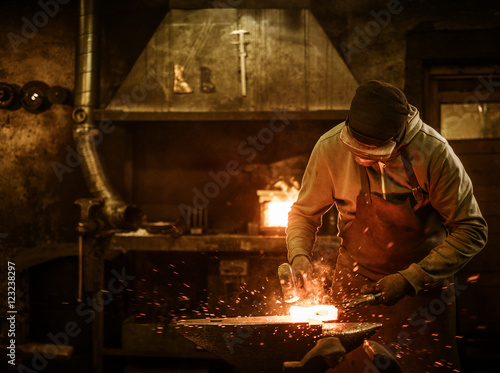 The blacksmith forging the molten metal on the anvil in smithy