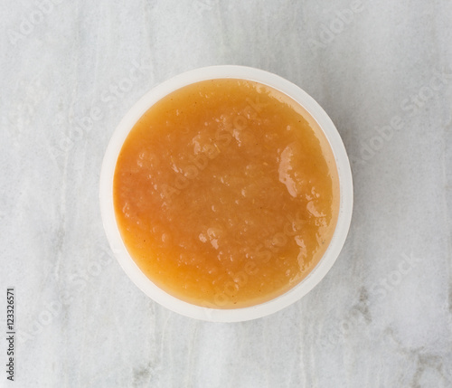 Cinnamon applesauce in a plastic container on a marble table top view.