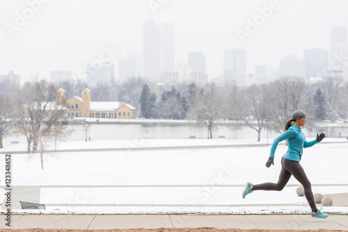 Woman running in winter through Denver Colorado City Park with skyline boathouse and snow in background