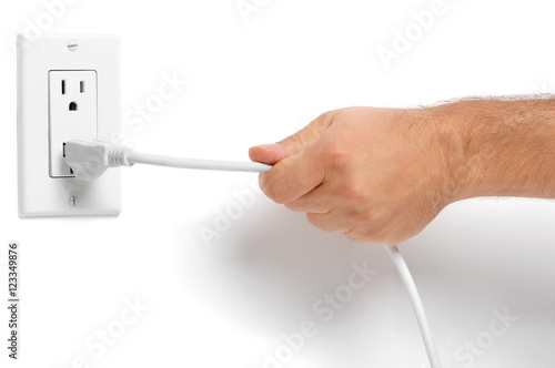 Man's hand pulling electrical plug from household wall socket outlet isolated on white background for use alone or as a design element