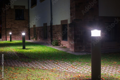 Outdoor lights (lanterns, bollards) in front of an old administration building illuminating a walkway in the garden at night 