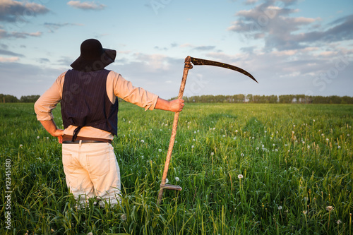 Farmer with a scythe on green field