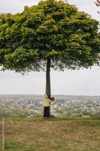 Little girl in the autumn park. hugging tree