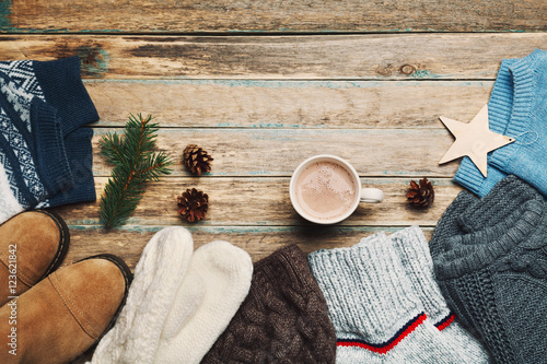 Autumn or winter clothes, sweater, shoes, mittens, fir tree and hot cocoa on wooden vintage background from above. Flat lay.