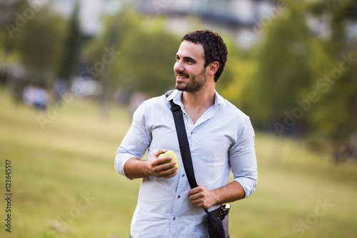 Young businessman is eating apple at the park.