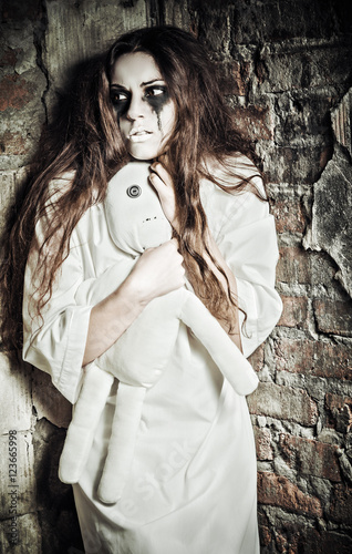 Horror scene: strange crazy girl with moppet doll in hands