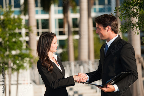 Attractive male female businessman and businesswoman shaking hands downtown outdoors with office building in background