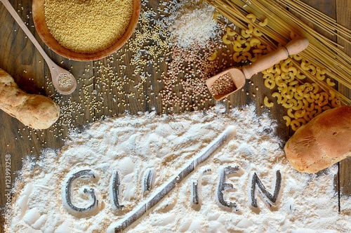 Gluten free cereals corn, rice, buckwheat, quinoa, millet, pasta and flour with scratched text gluten on brown wooden background