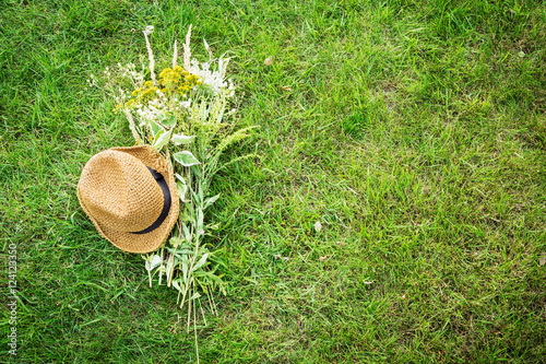 Straw hat and wild-flower bunch on green grass lawn