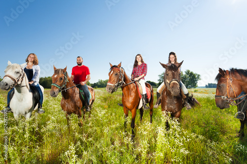Happy equestrians riding horses in summer field