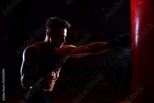 Young male boxer hitting punching bag on black background.