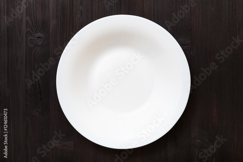 top view of white deep plate on dark brown table